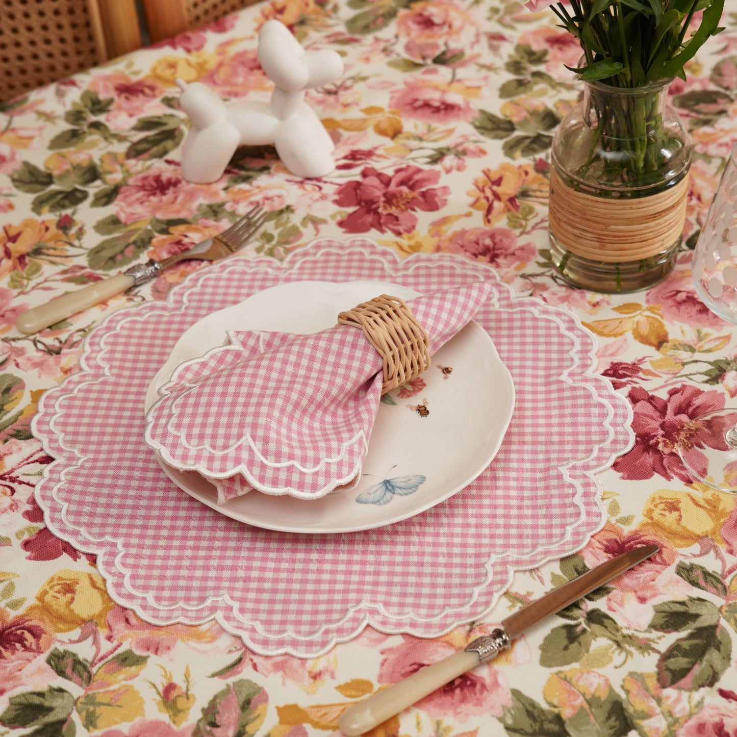 Dining table setting with floral tablecloth, plates, cutlery, and decorative items.