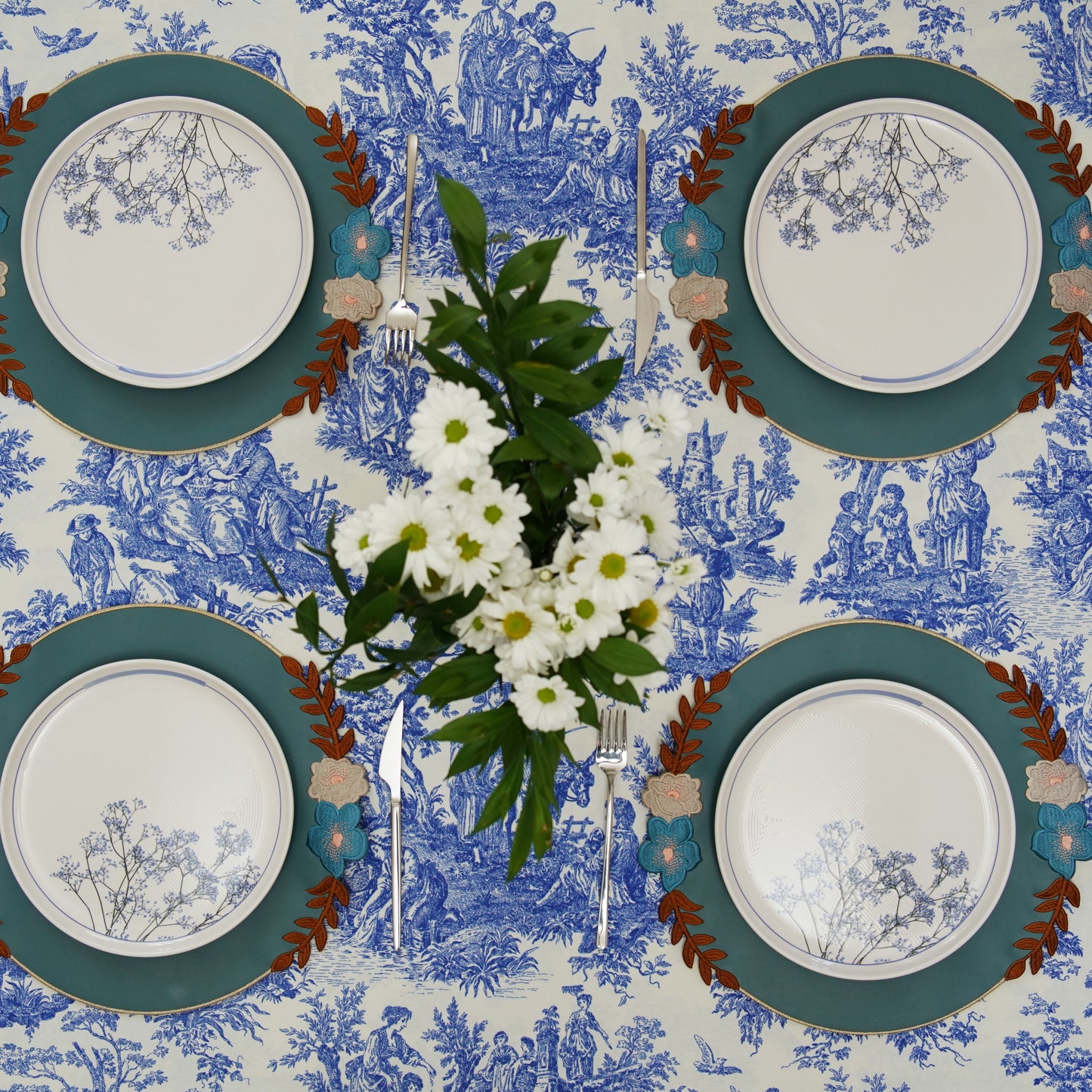 Set of four plates with decorative borders on a blue and white patterned tablecloth.