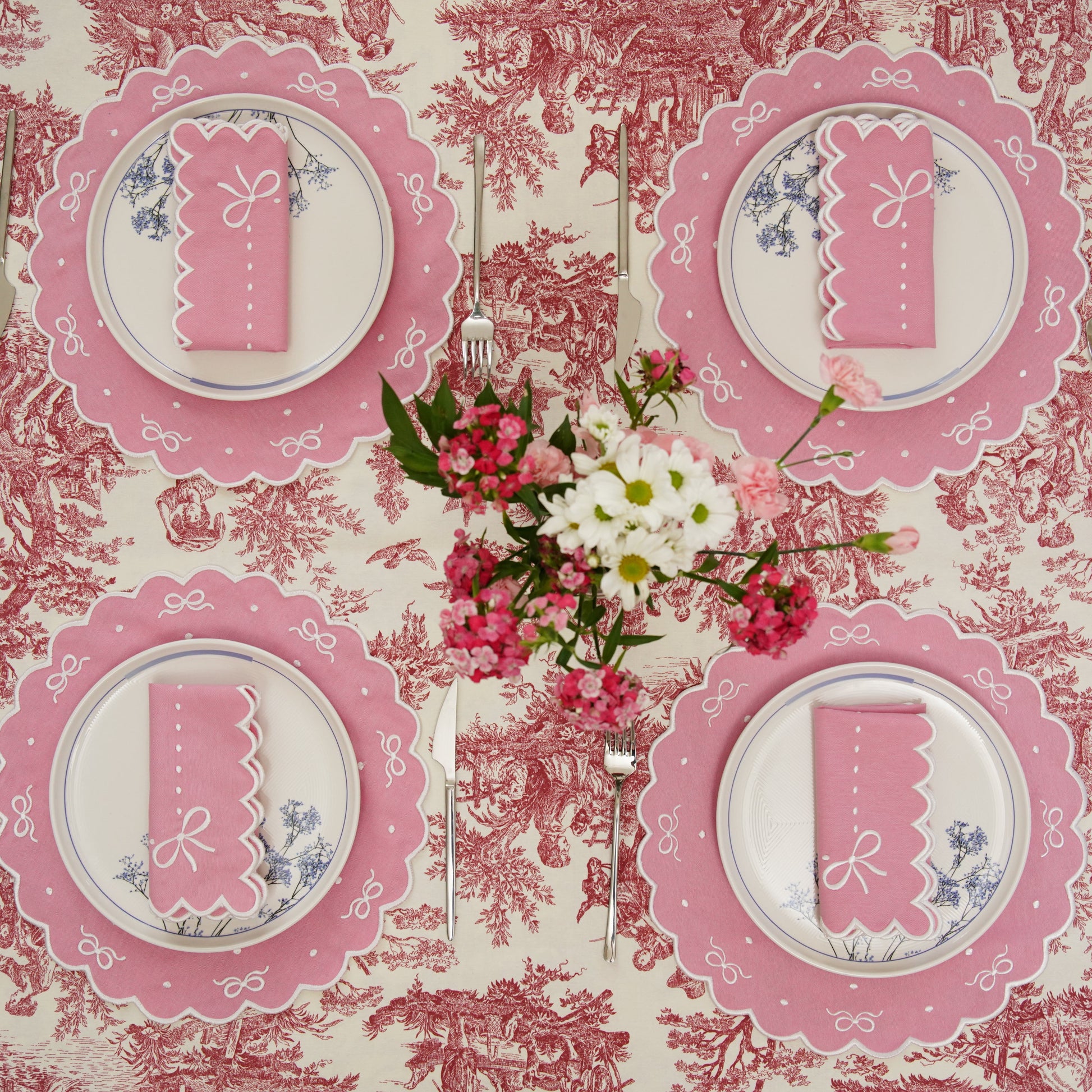 Table setting with pink plates and napkins on a floral tablecloth