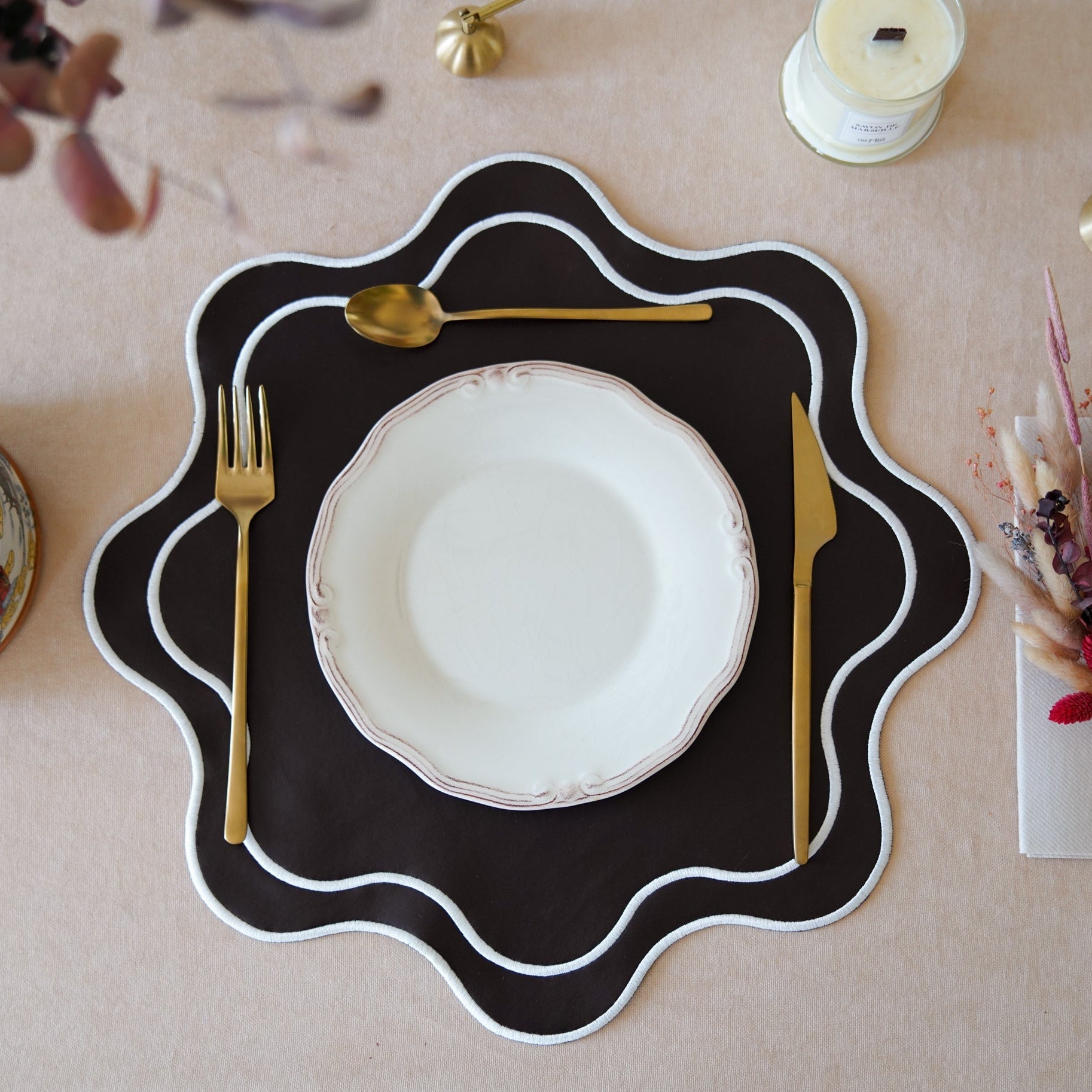 A brown faux leather placemat with a cut-out shape, featuring embroidery details around the edge, displayed on a table with a white plate and cutlery in the center.
