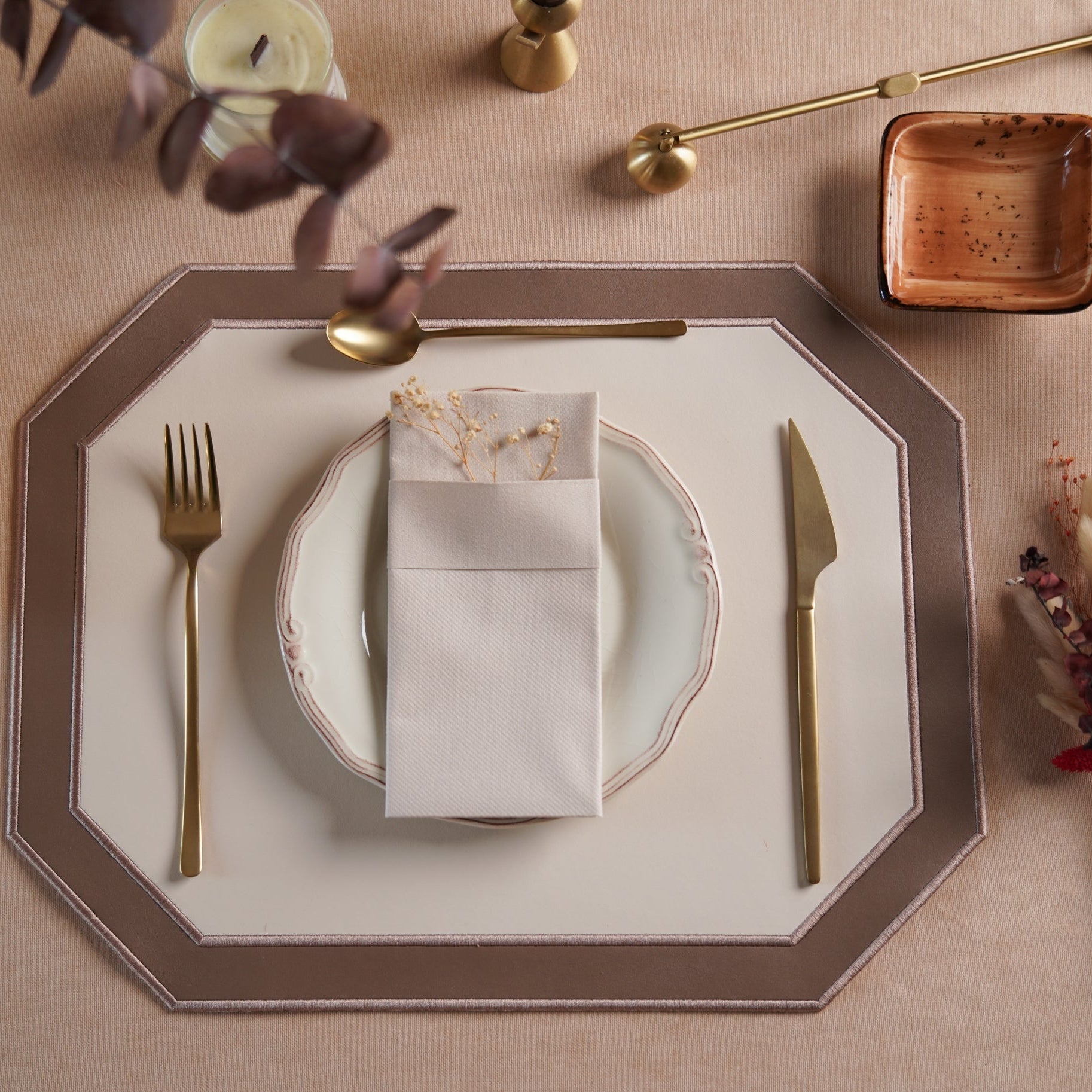 A white and light brown faux leather placemat with embroidered details, presented on a table setting with cutlery and a plate.