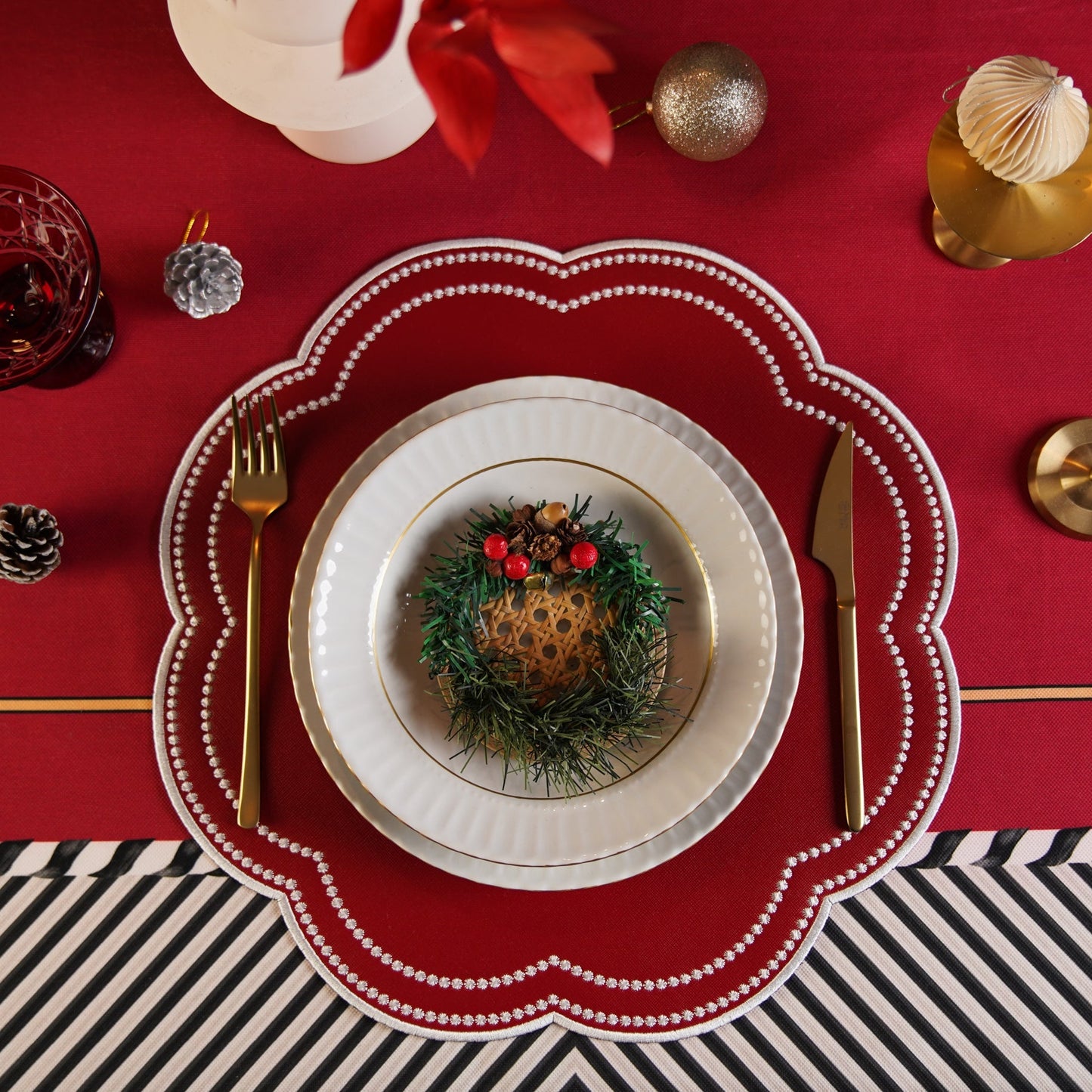 A red faux leather placemat with a decorative pattern, placed on a dining table setting with cutlery and a glass.