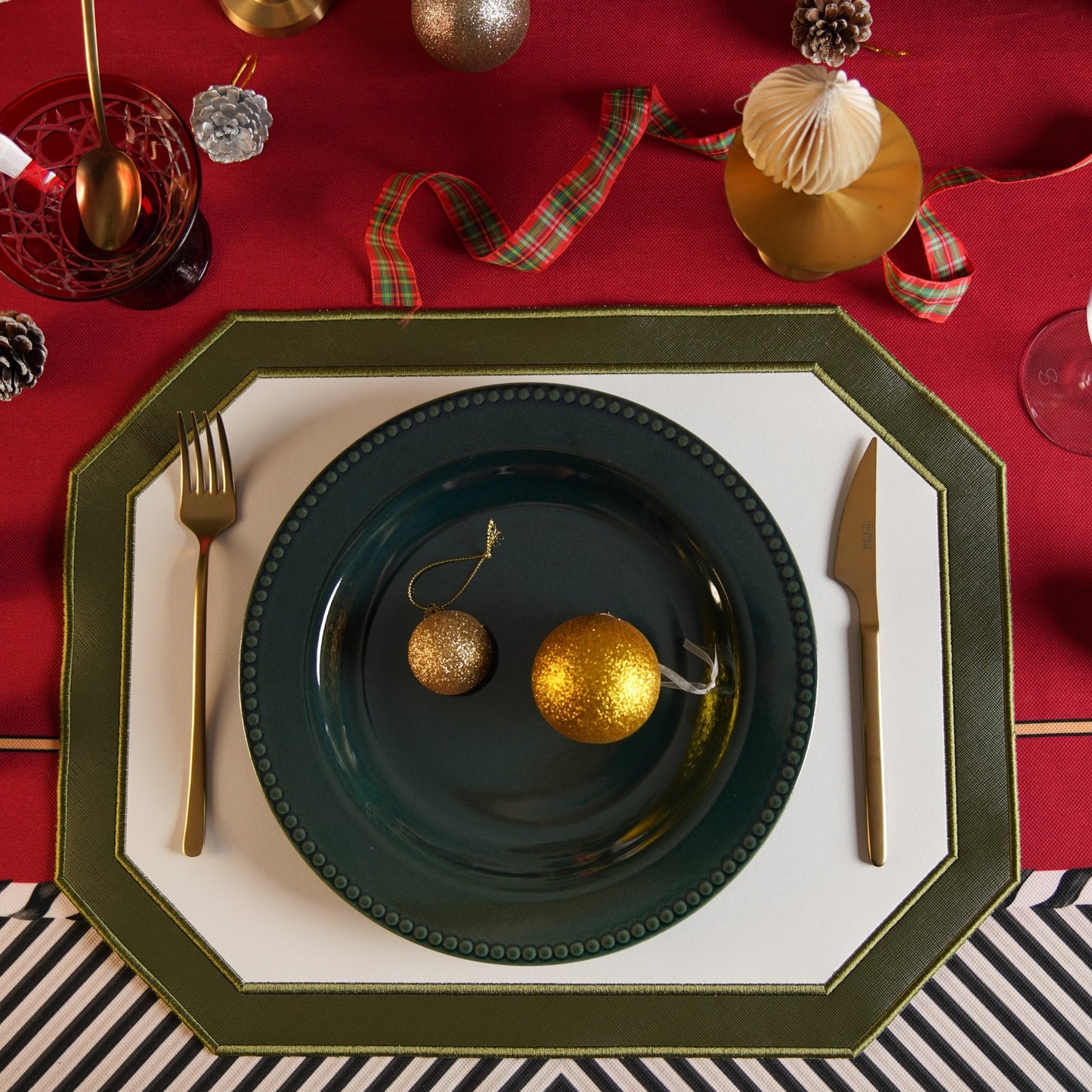 Christmas-themed table setting with gold ornaments on a red tablecloth.
