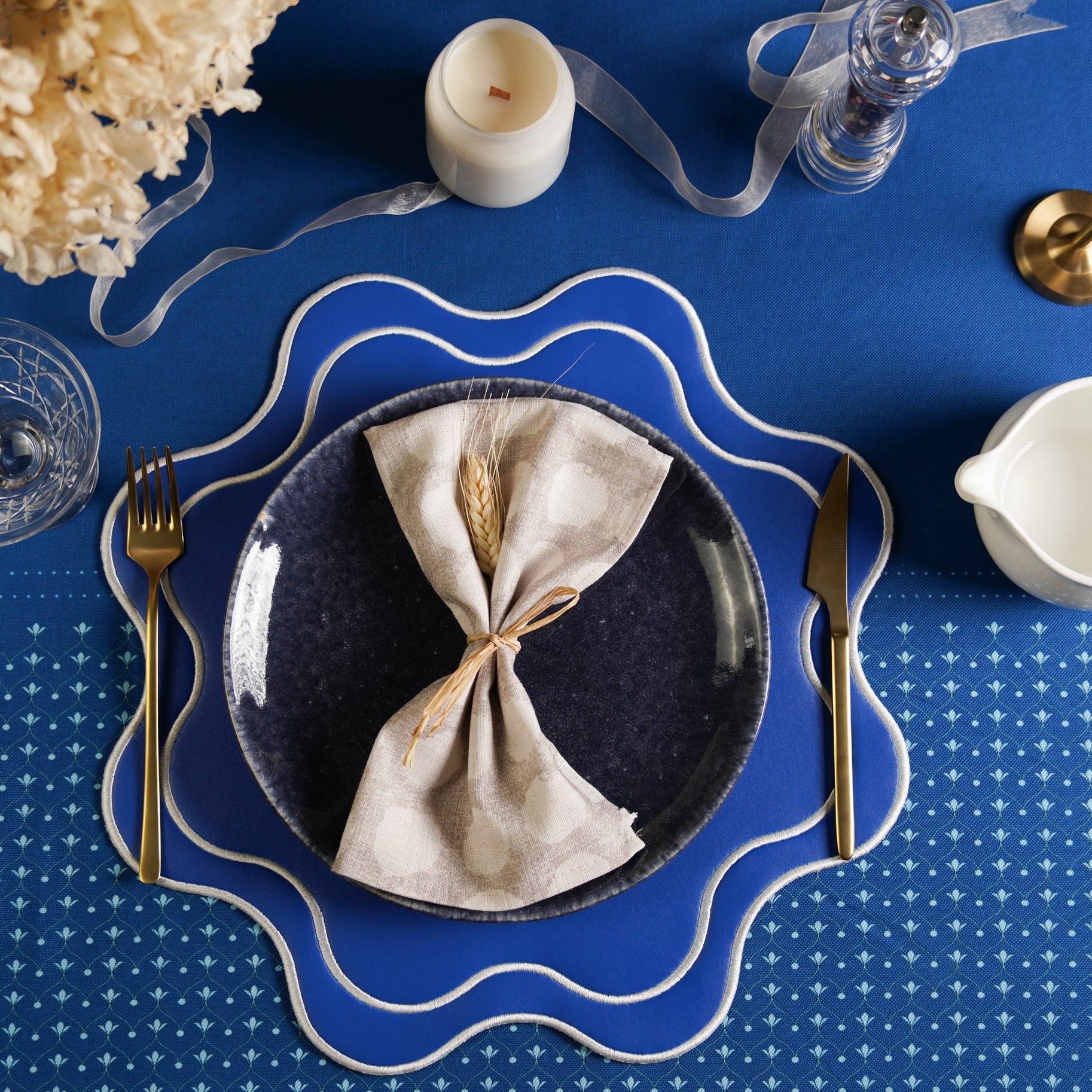 A blue faux leather placemat with a decorative pattern, presented on a table setting with a plate, cutlery, and a white napkin.