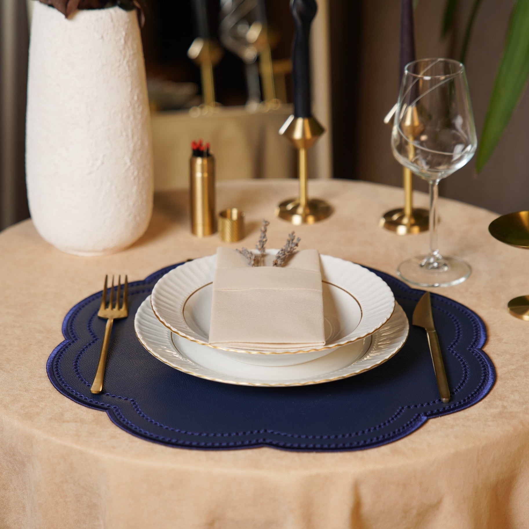 Elegant table setting with white plates, gold cutlery, and a blue placemat on a beige tablecloth.