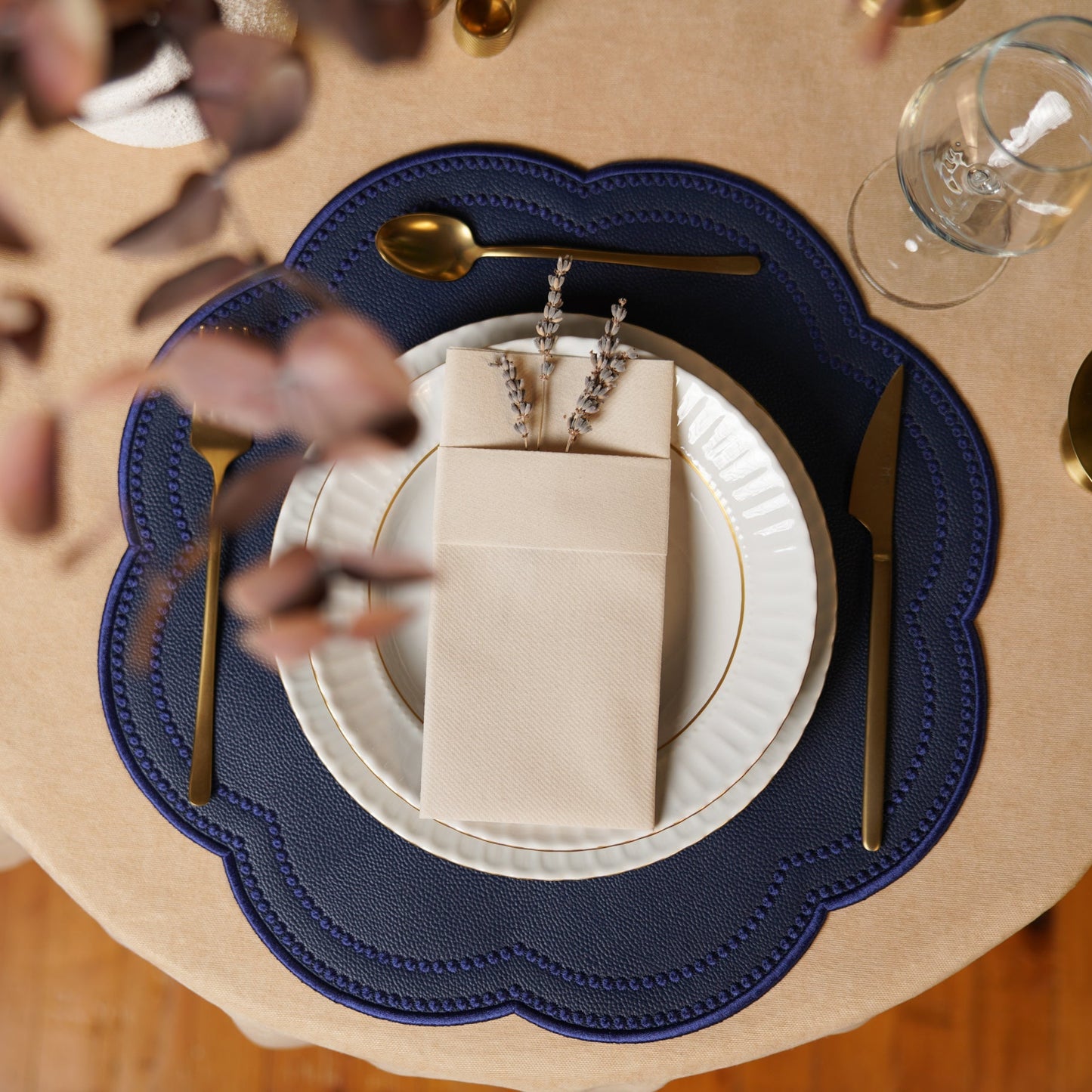 Elegant table setting with a blue placemat, white plate, gold cutlery, and beige napkin.