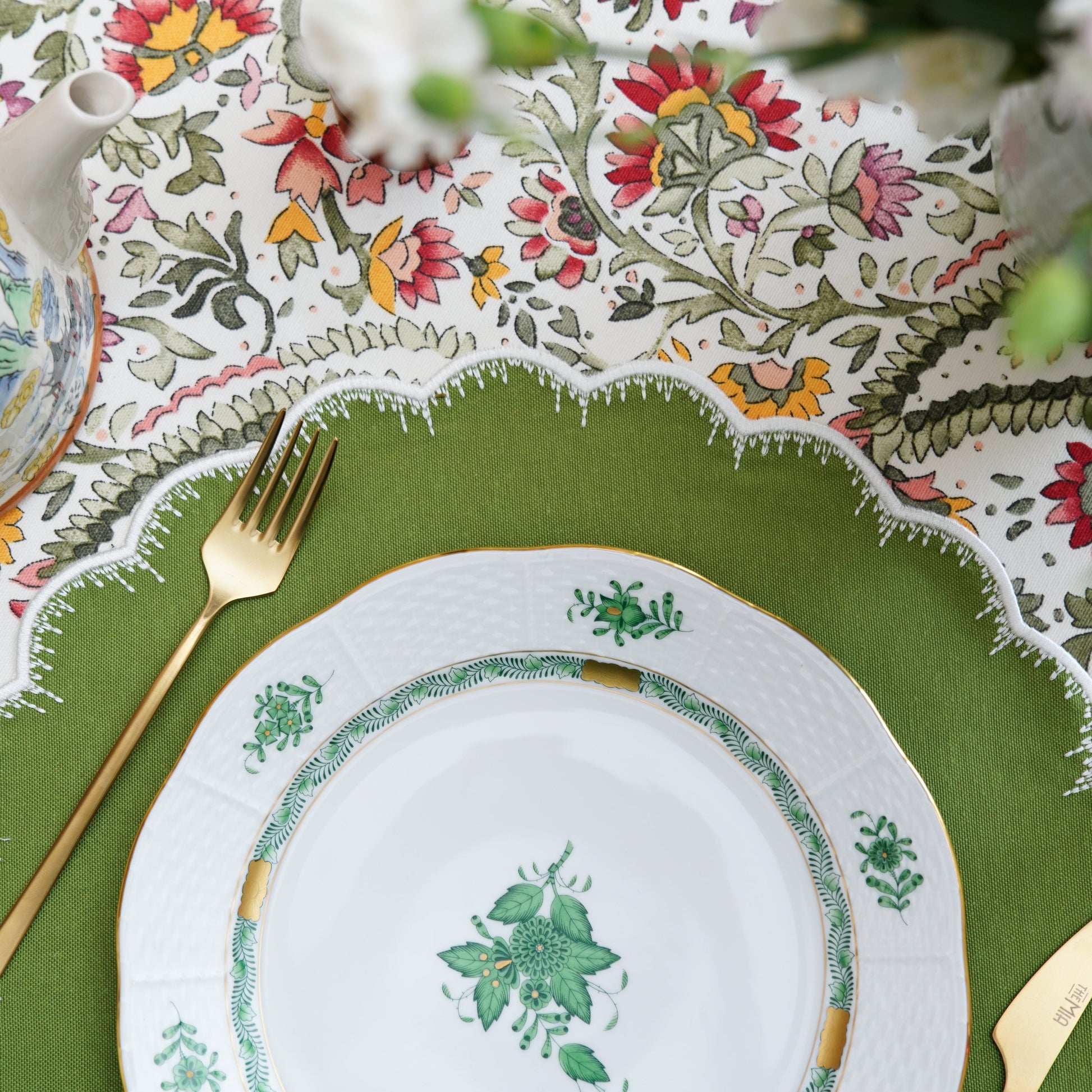 Decorative table setting with a green plate, gold fork, and floral-patterned tablecloth.