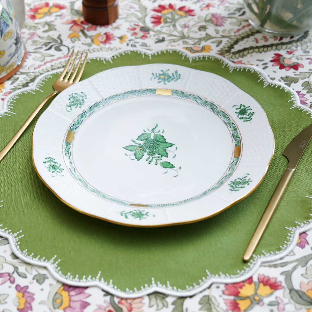 Set table with a plate, cutlery, and green placemat on a patterned tablecloth.