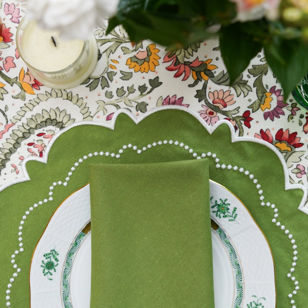 Decorative table setting with green napkin and placemat on a floral tablecloth.