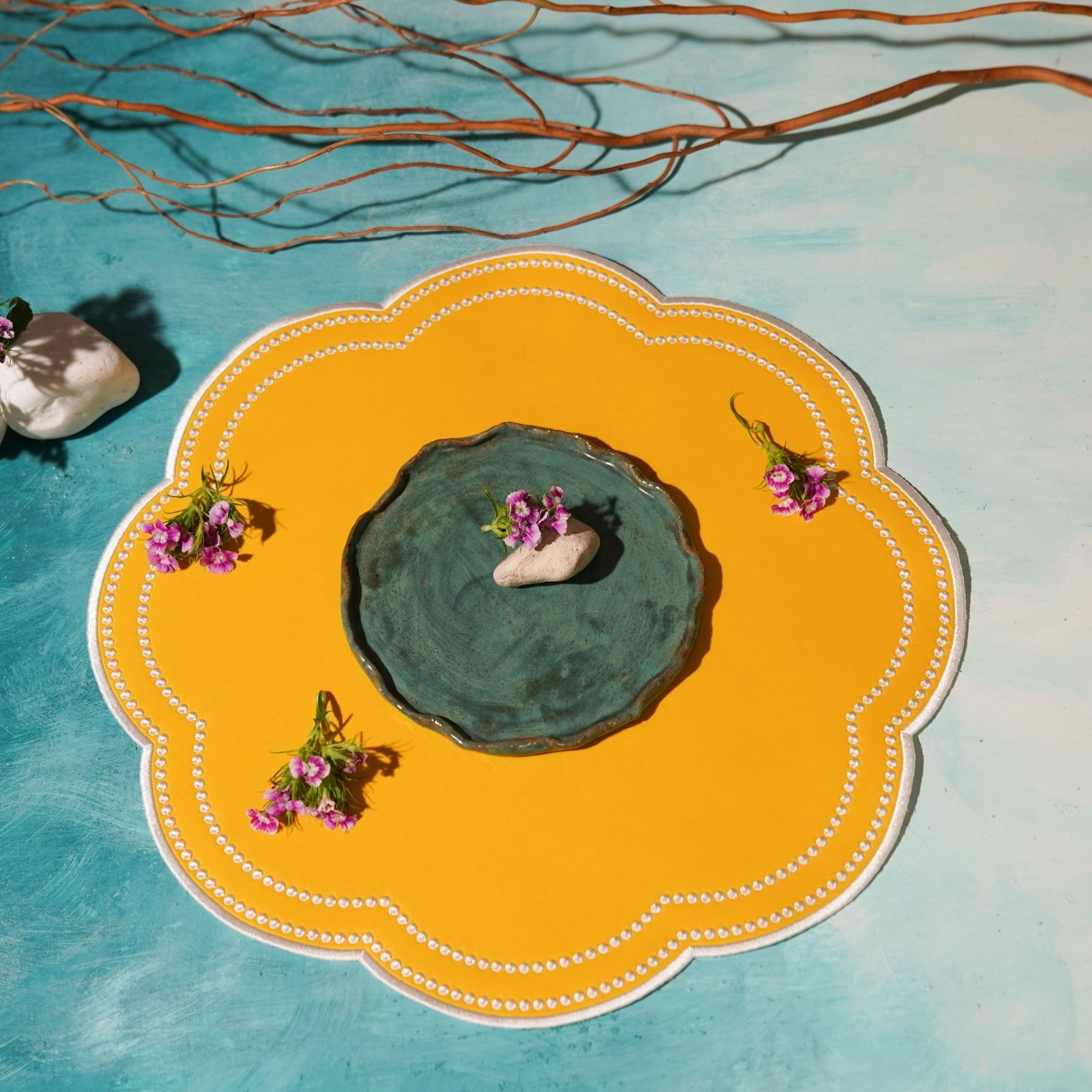 Decorative yellow plate with a central green dish, surrounded by small plants and stones on a blue and white gradient background.