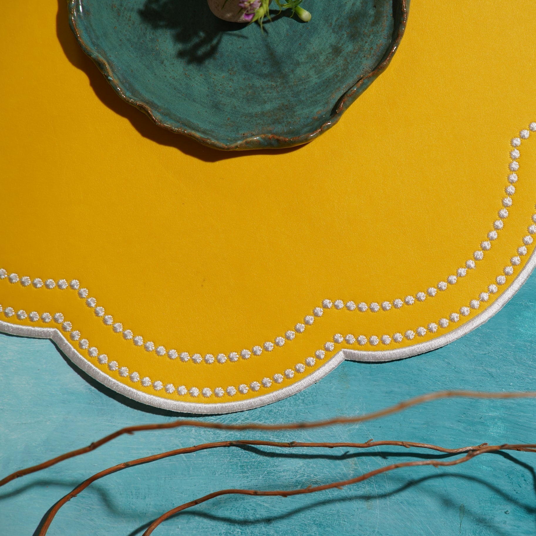 Round turquoise coaster with decorative edge on a yellow and blue background