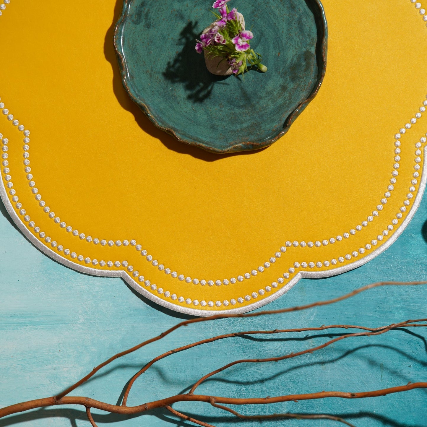 Yellow plate with a blue center and decorative edge, featuring a small plant, on a teal background.