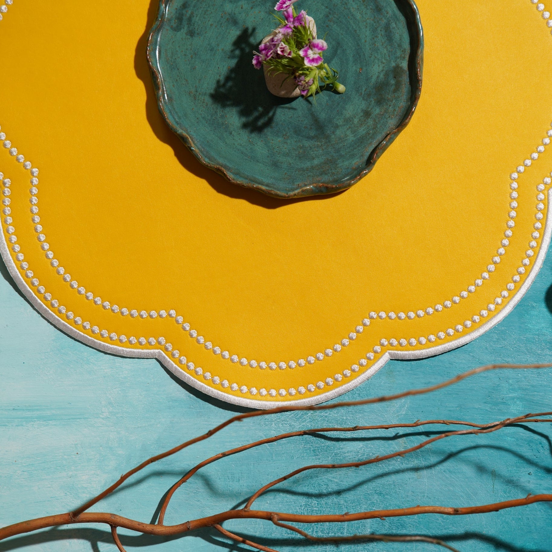 Yellow plate with a blue center and decorative edge, featuring a small plant, on a teal background.