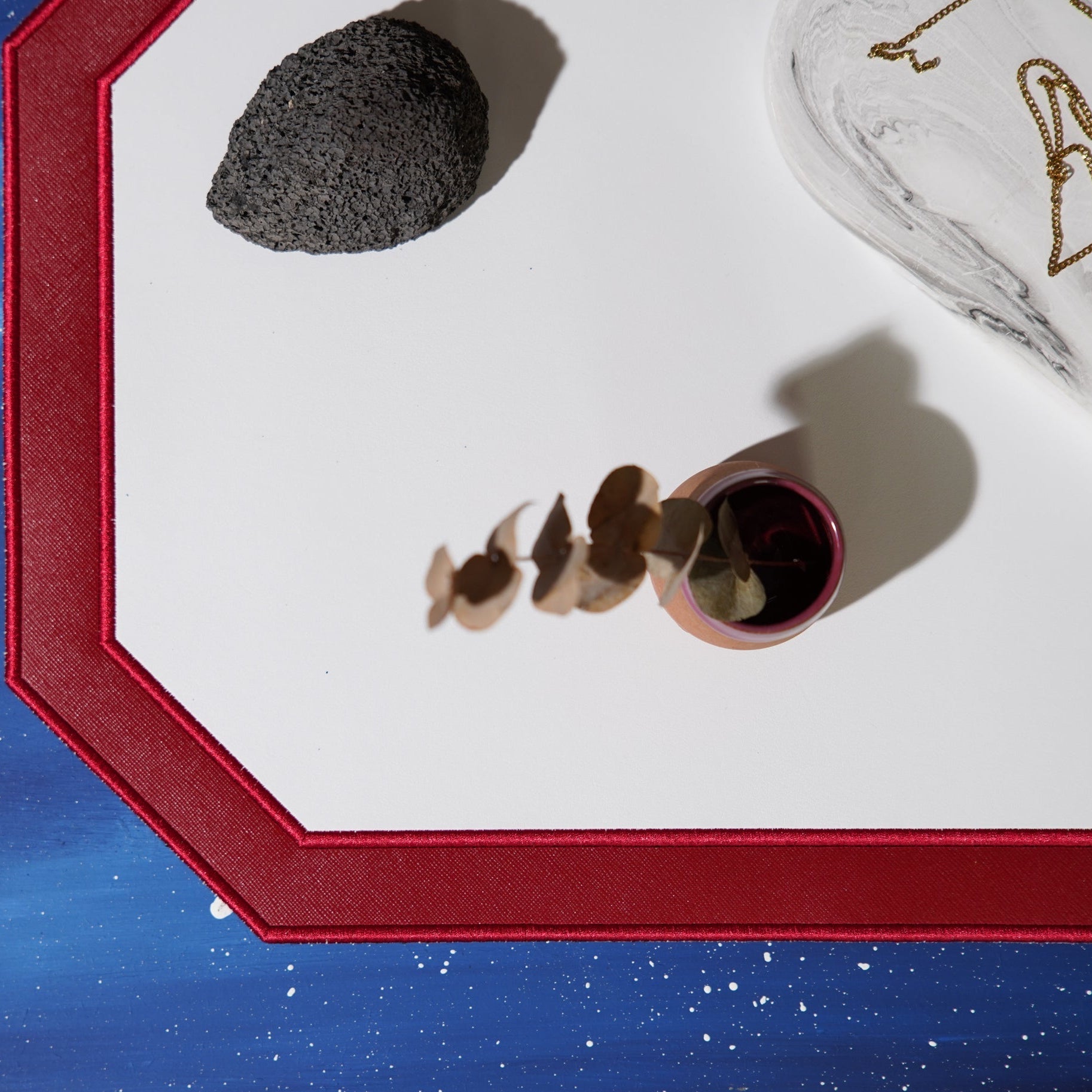 Decorative setting with a red frame, black stone, and small vase on a white surface.