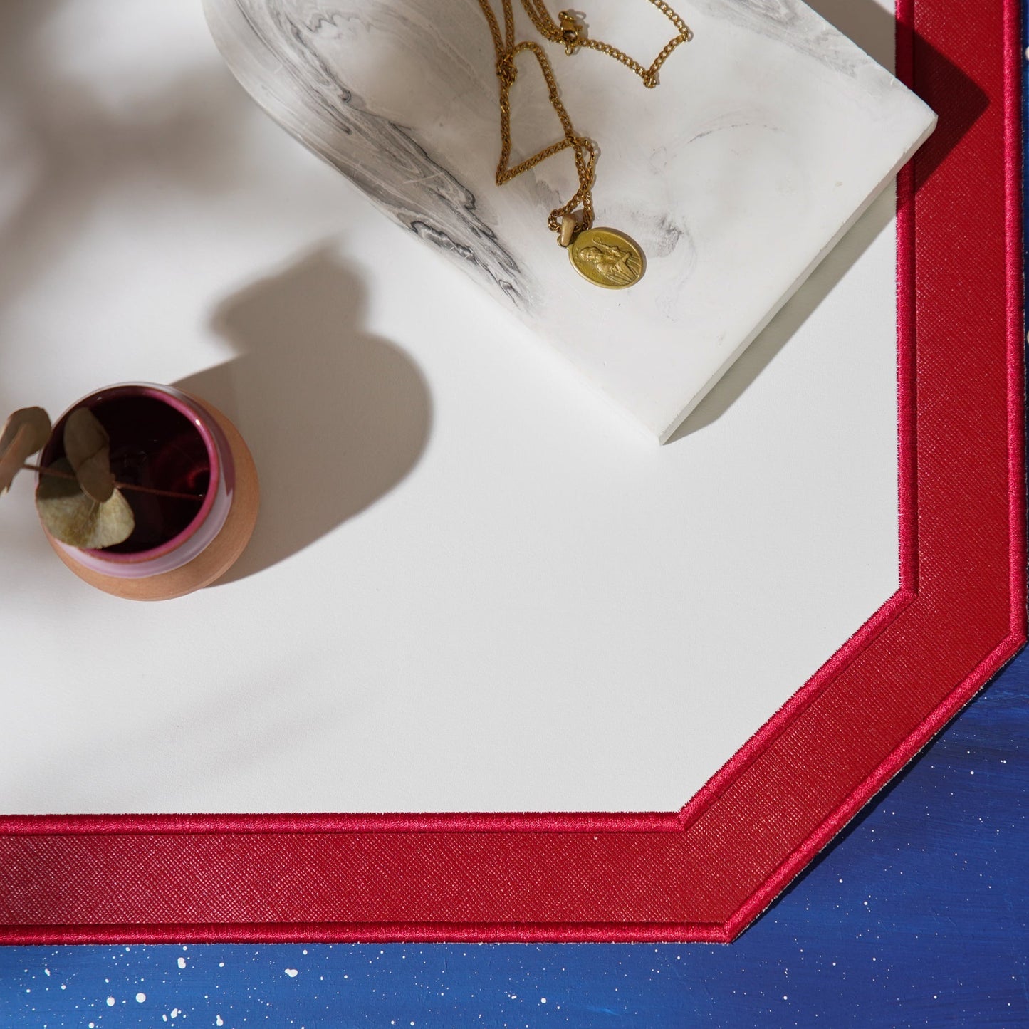 Close-up of a red-framed picture with a necklace and small container on a white surface.