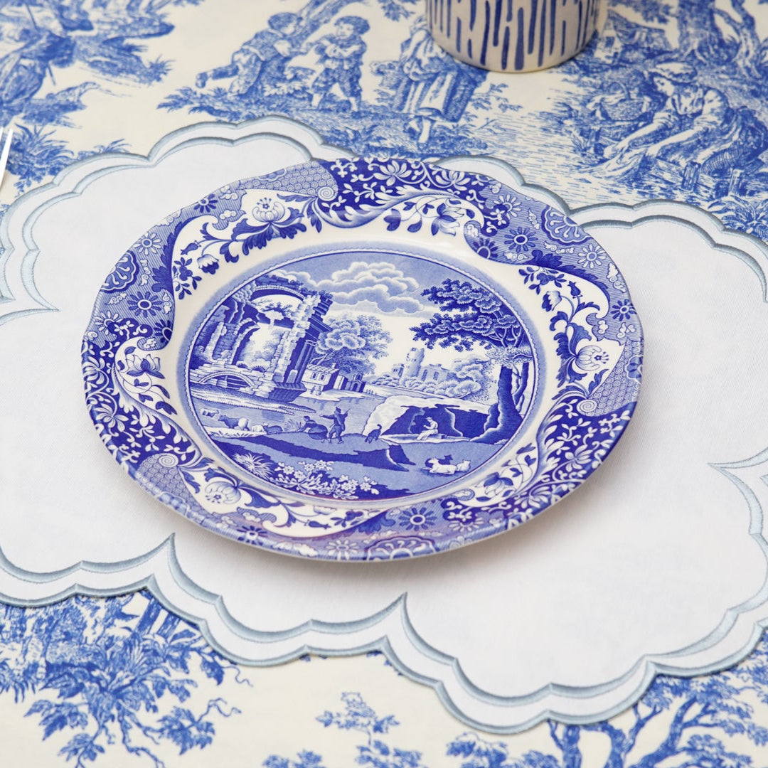 Blue and white patterned table setting with a decorative plate on a matching tablecloth.