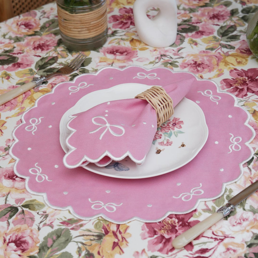 Table setting with pink decorative plate and cutlery on a floral tablecloth.
