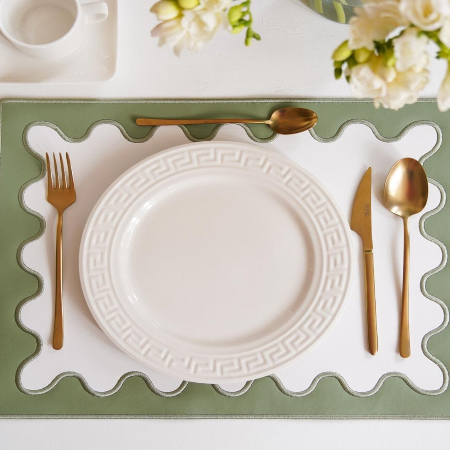 A white plate on a green faux leather placemat with gold cutlery on either side, set against a dining table backdrop.