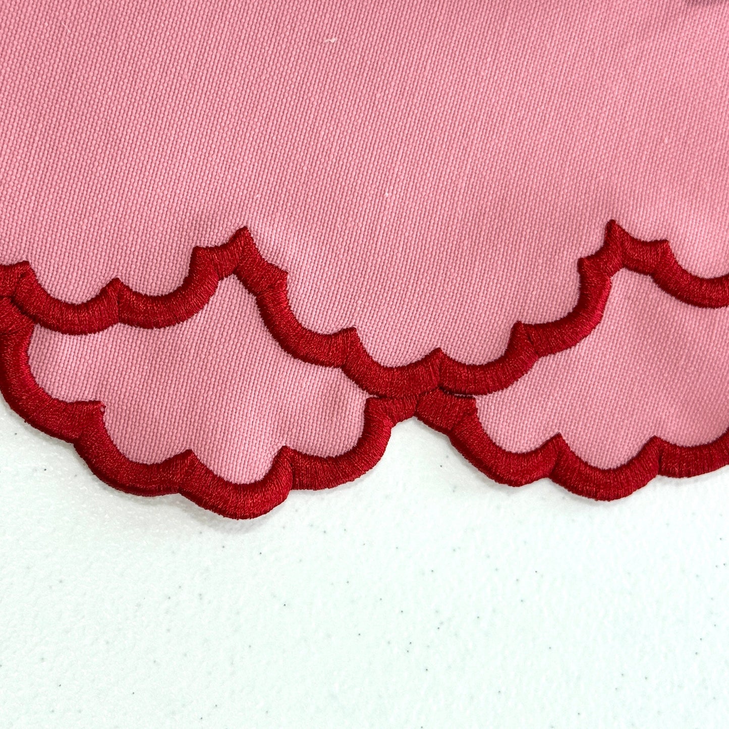 Pink fabric with red scalloped edge on a white background