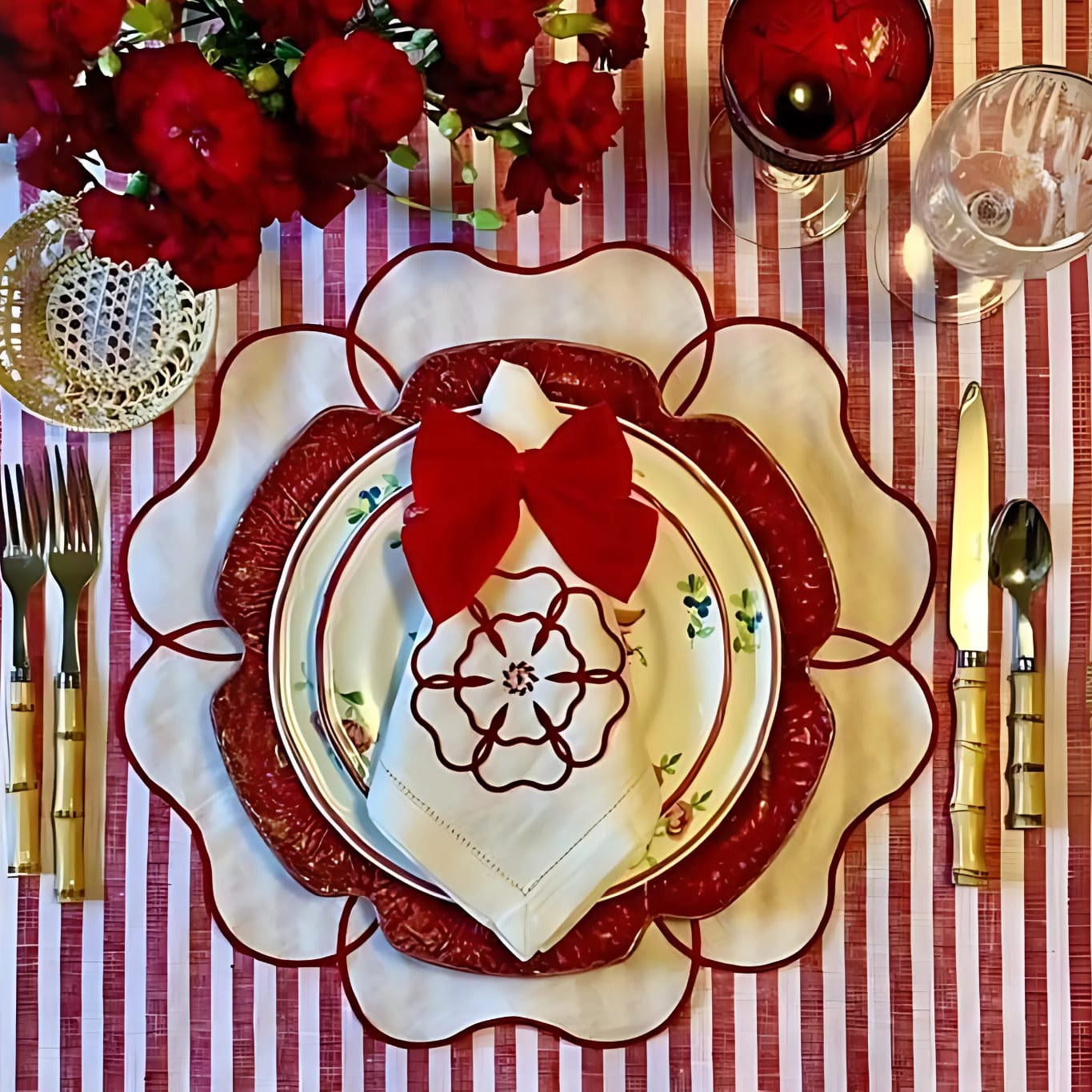 A set of red and ivory embroidered placemats and napkins on a dining table, with a Christmas tree and decorative red bow in the background.