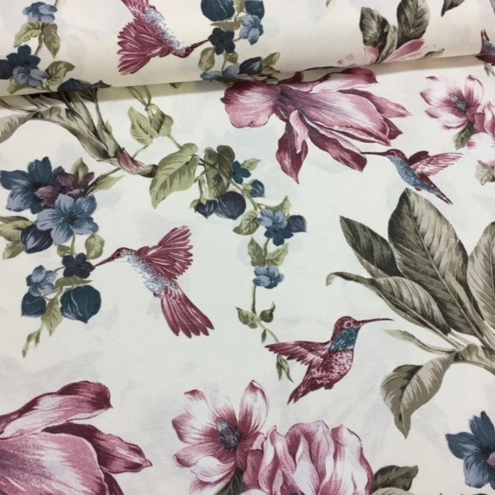 A rectangular tablecloth with a floral and bird pattern in pink, blue, and green colors on a white background.