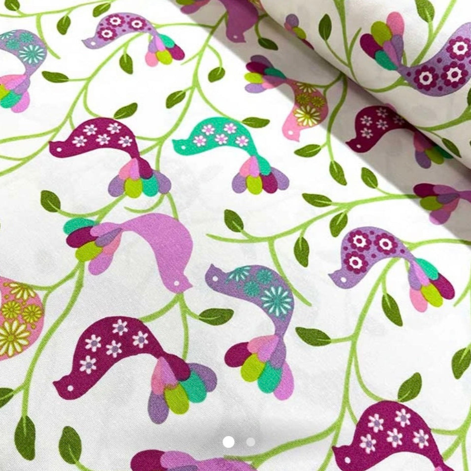 A rectangular tablecloth with a purple bird print on a white background, featuring green leaves and multicolored flowers.