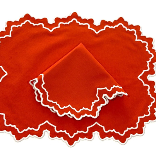 A set of orange fabric placemats with a white embroidered edge on a white background.