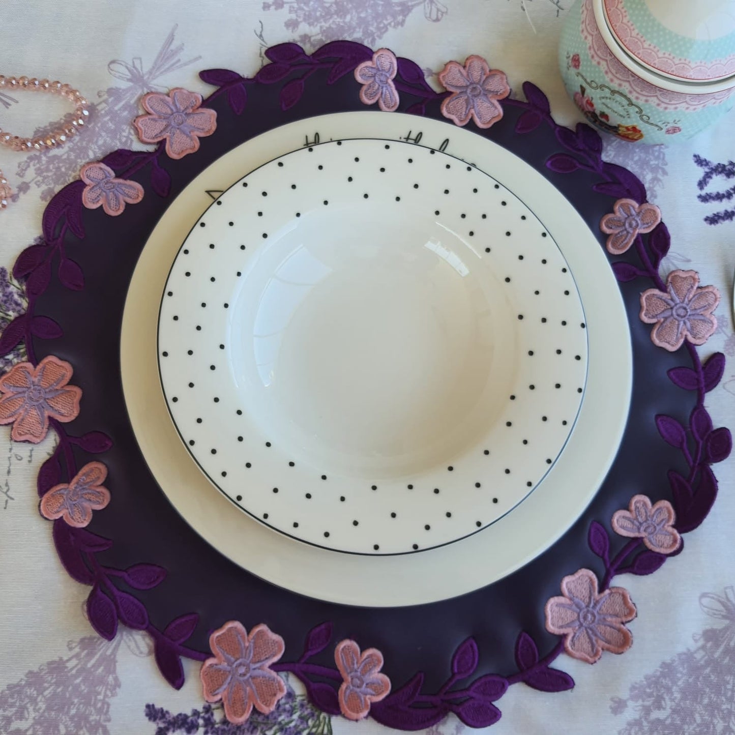 Decorative place setting with a floral placemat on a tablecloth.