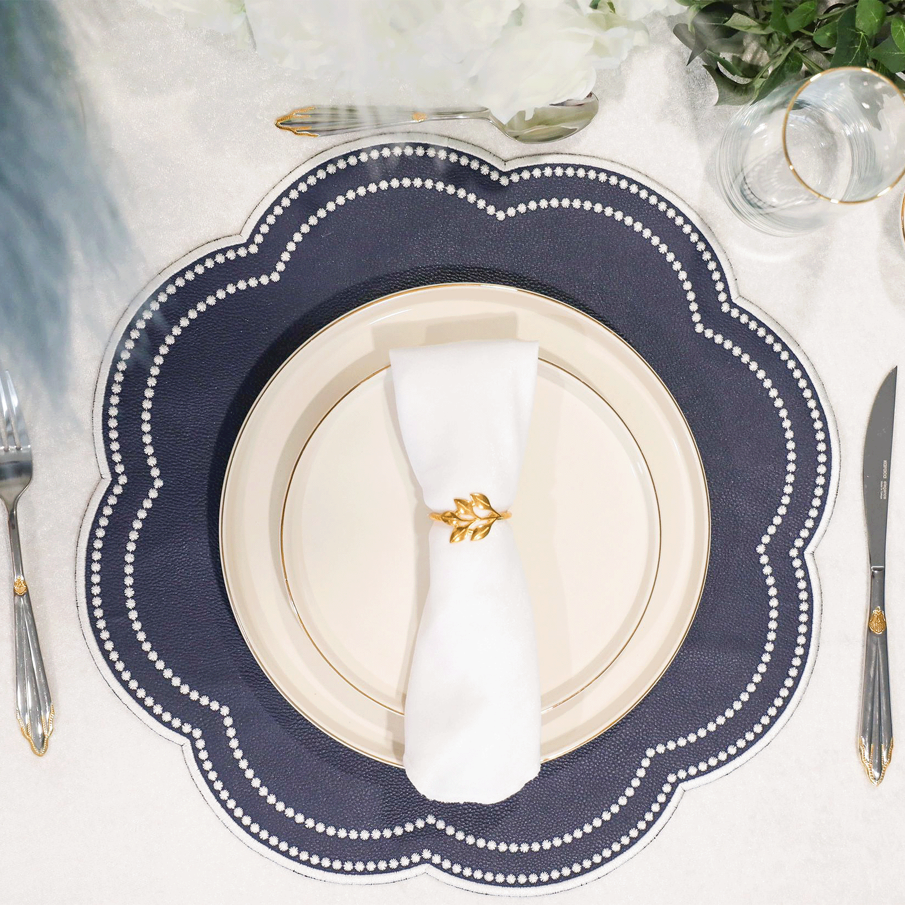 Elegant table setting with a navy blue plate, white napkin, and gold cutlery on a white tablecloth.