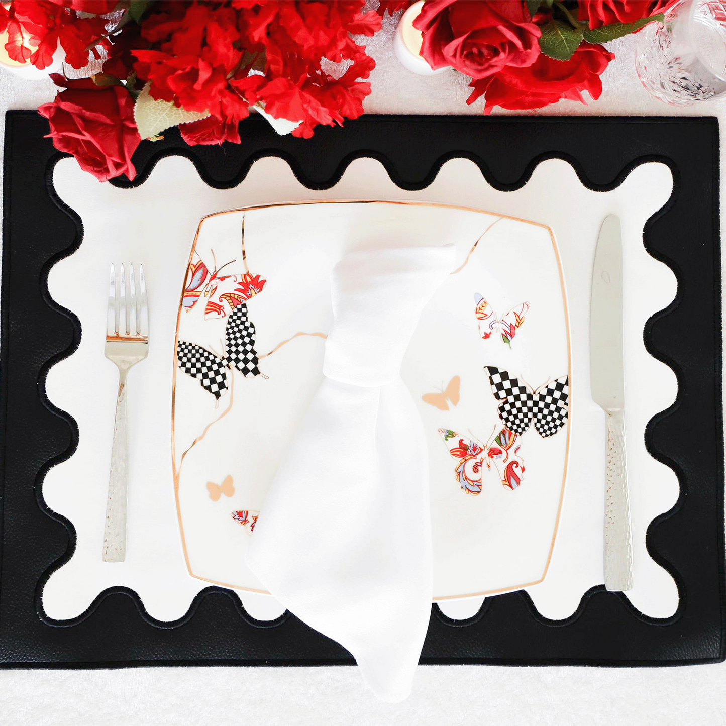 A black faux leather placemat with white embroidered details around the edge, displayed on a table with a white plate and silverware in the center.