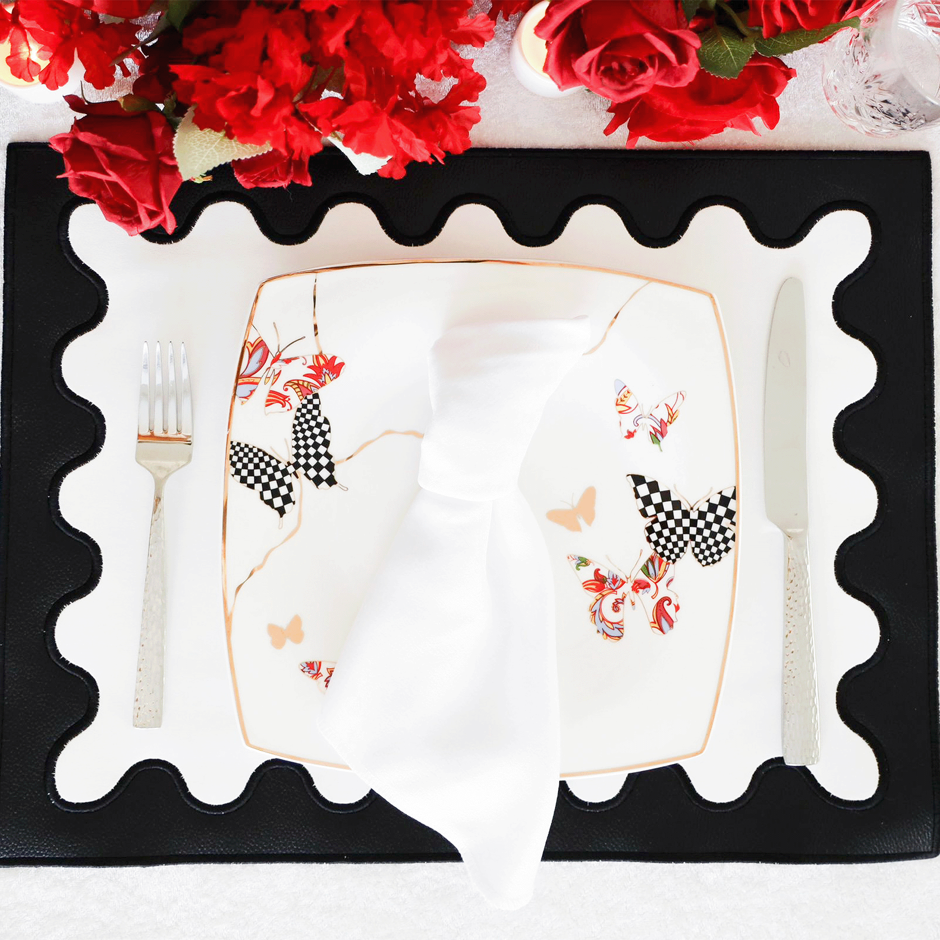 A black faux leather placemat with white embroidered details around the edge, displayed on a table with a white plate and silverware in the center.