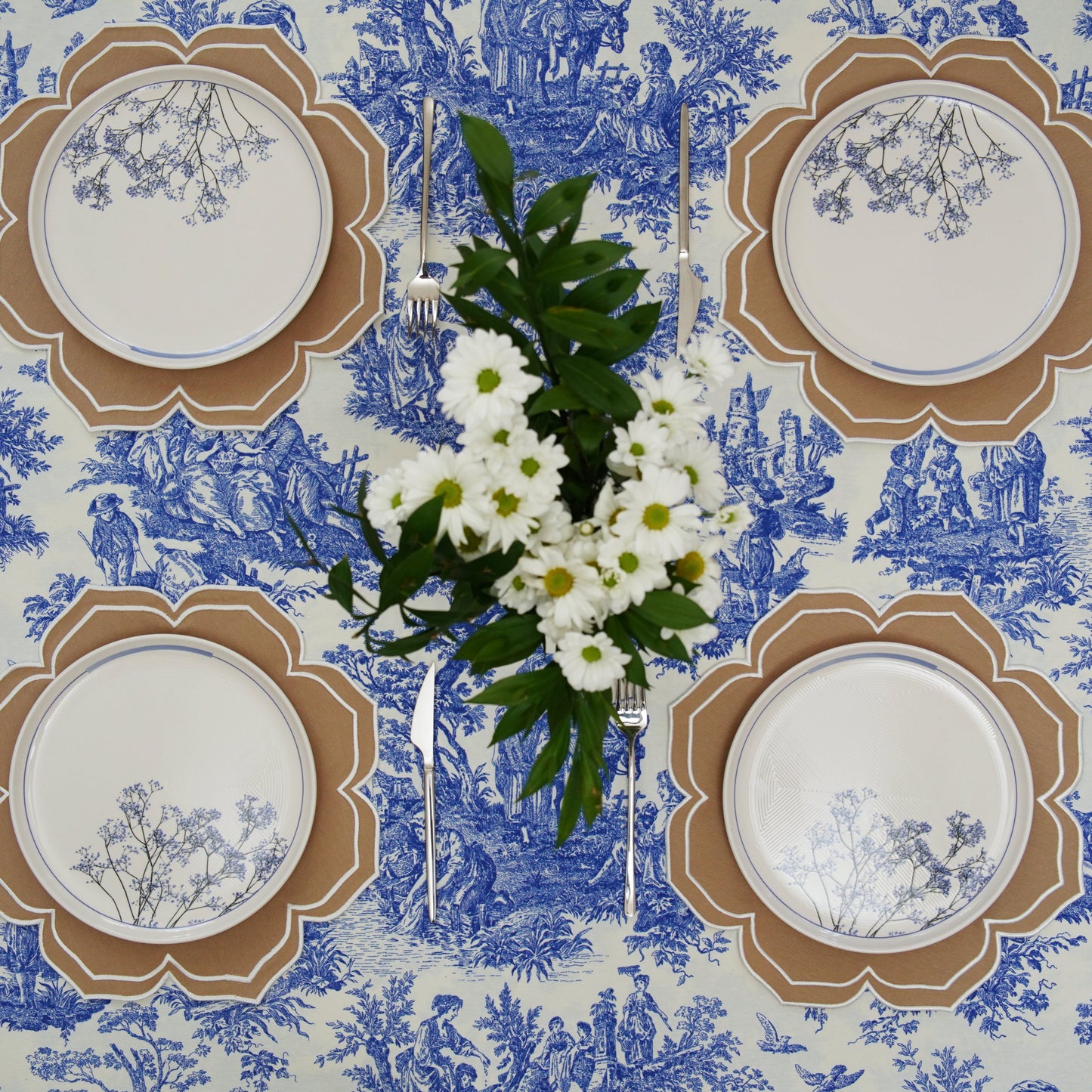 Table setting with white plates, silverware, and a bouquet of flowers on a blue and white toile tablecloth.