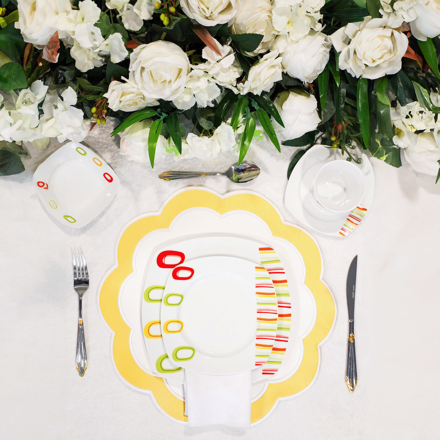 A set table with a white and yellow faux leather placemat, surrounded by silverware and a floral arrangement.