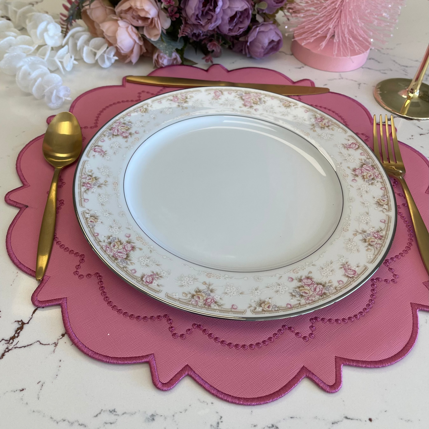 Decorative table setting with a white plate, pink placemat, and floral arrangement on a marble surface.