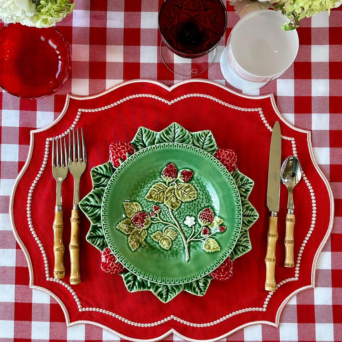Decorative table setting with a green plate, red placemat, and floral arrangements on a checkered tablecloth.
