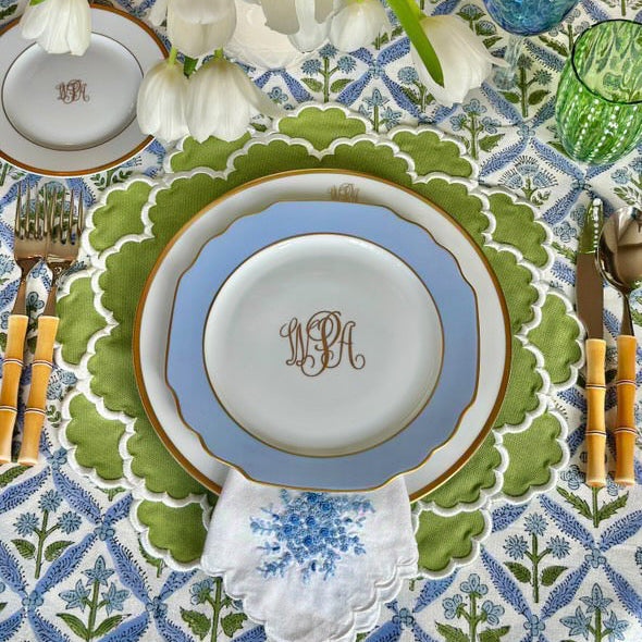 Decorative table setting with monogrammed plates, cutlery, and flowers on a patterned tablecloth.