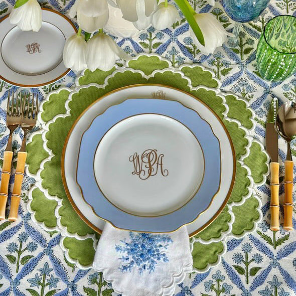 Decorative table setting with monogrammed plates, cutlery, and flowers on a patterned tablecloth.