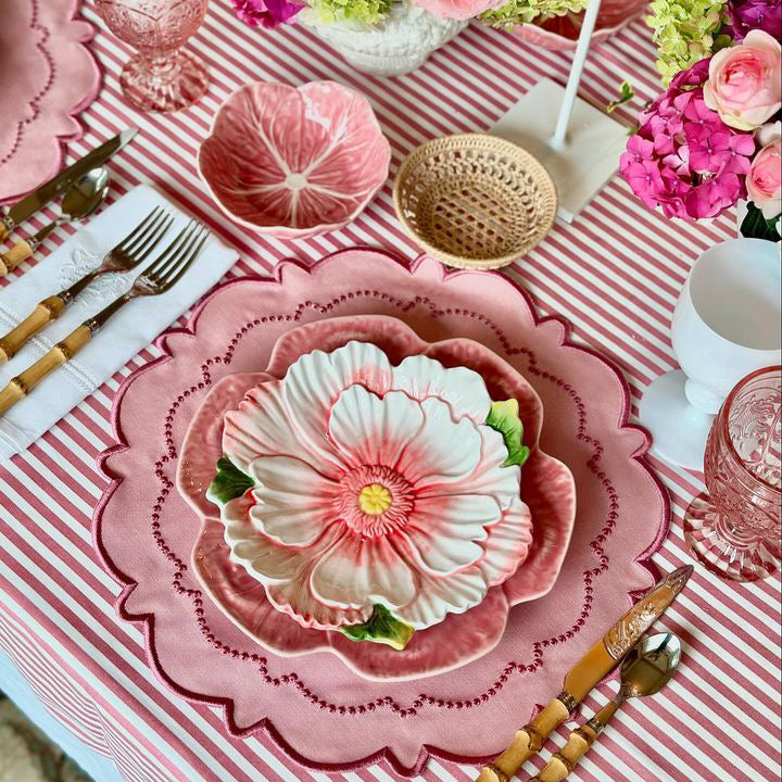 Decorative table setting with floral plates, pink and white striped tablecloth, and colorful flowers.