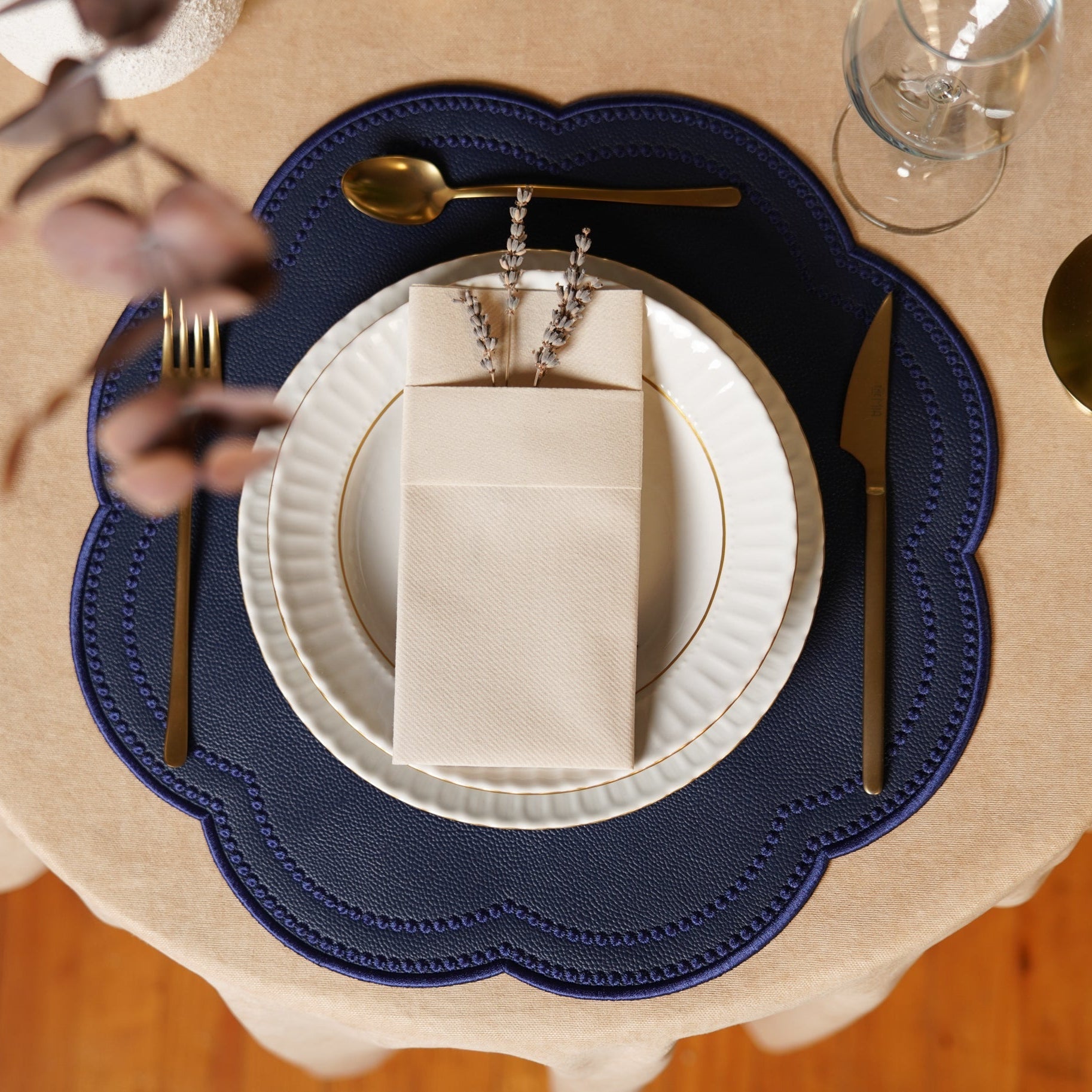 Dining table setting with a blue placemat, white plates, gold cutlery, and a beige napkin.