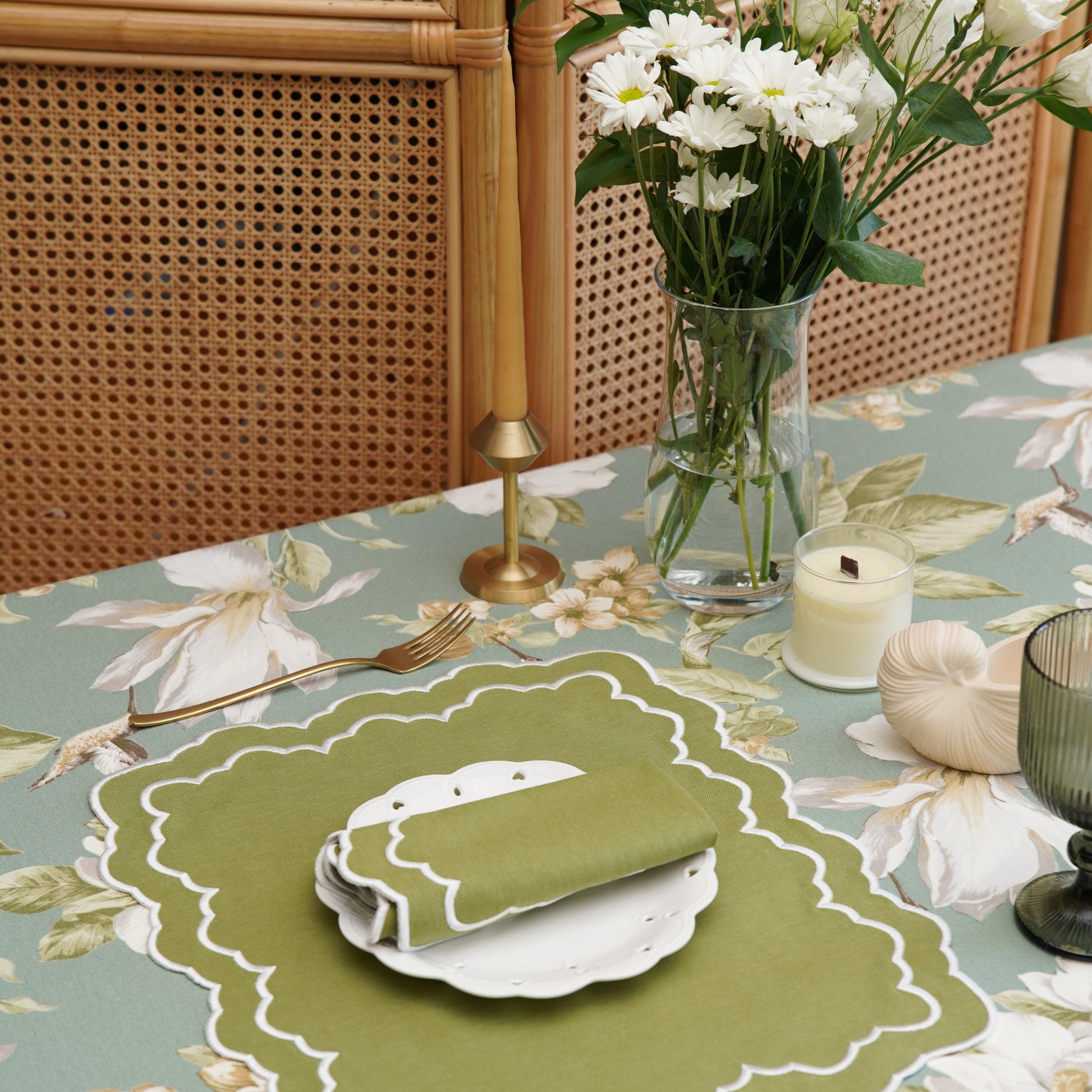 Set table with floral tablecloth, green placemat, and white flowers in a vase.