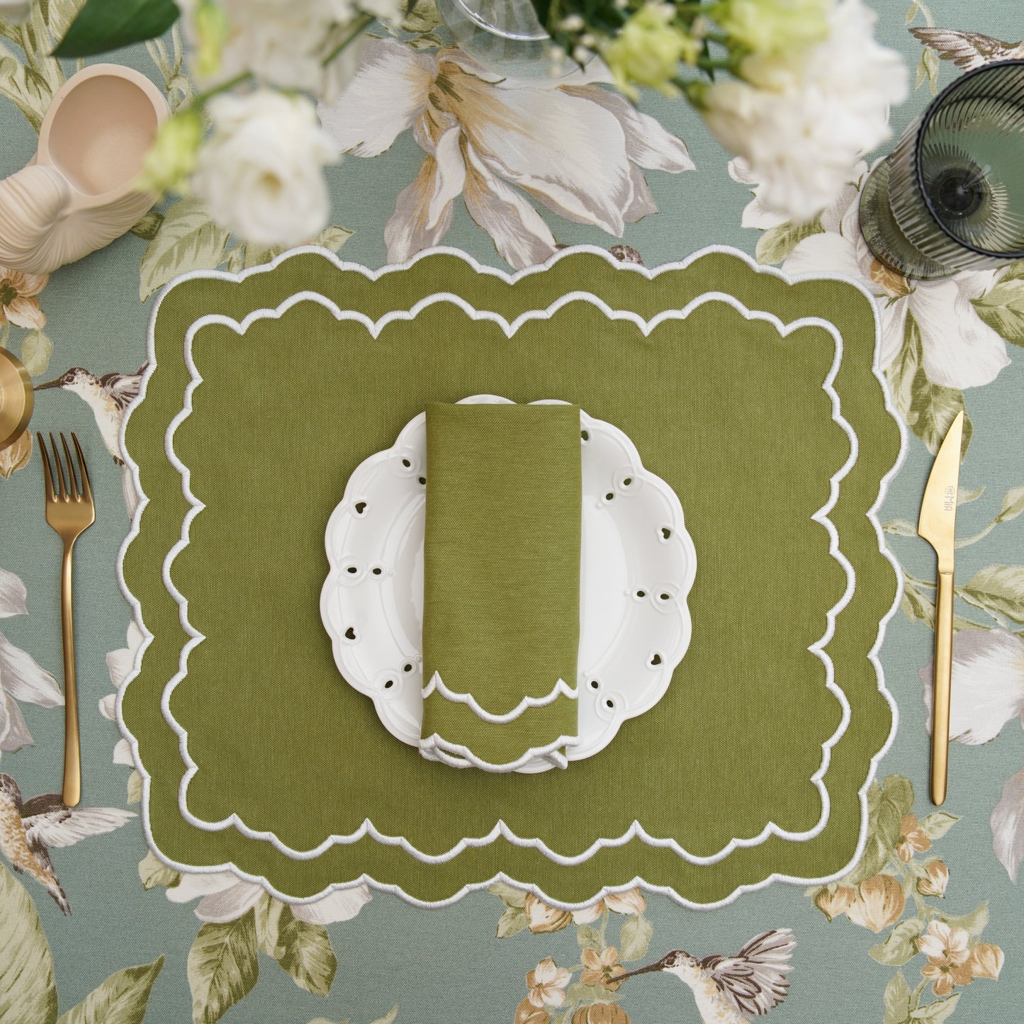 Green placemat with cutlery on a floral tablecloth
