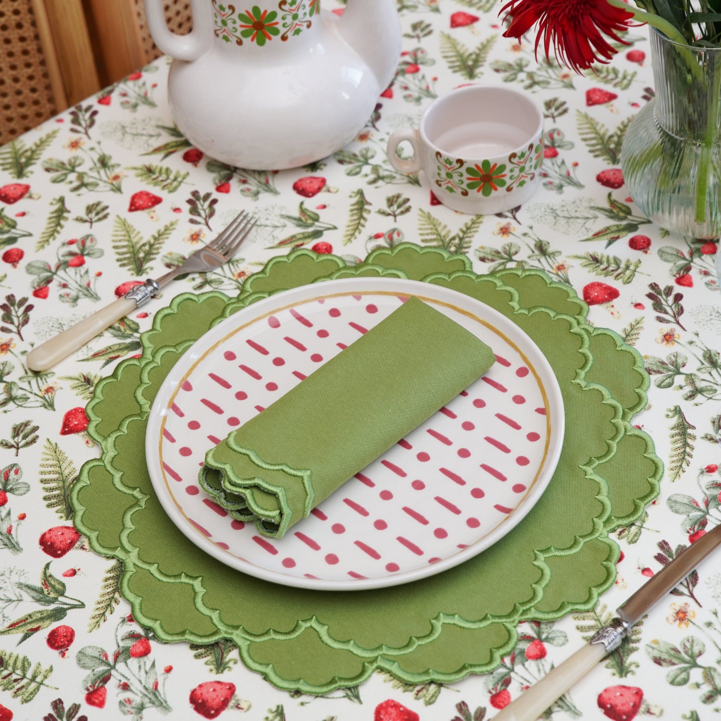 Table setting with a teapot, plates, and flowers on a floral tablecloth.