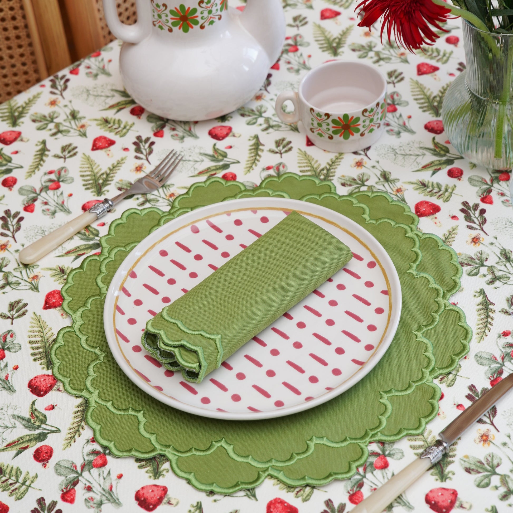 Table setting with a teapot, plates, and flowers on a floral tablecloth.