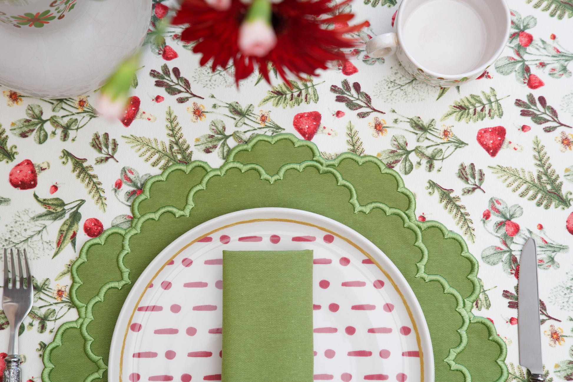 Table setting with a floral tablecloth, green placemat, and red napkin.