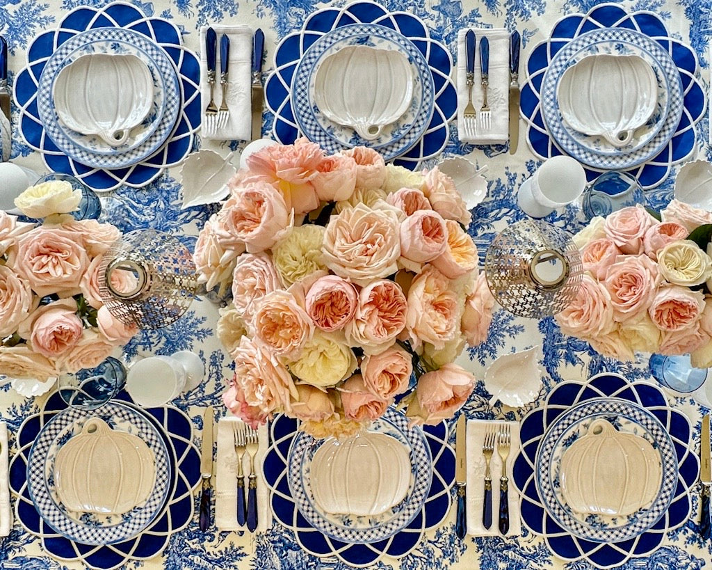Elegant table setting with blue and white patterned plates, pink flowers, and silverware on a matching tablecloth.