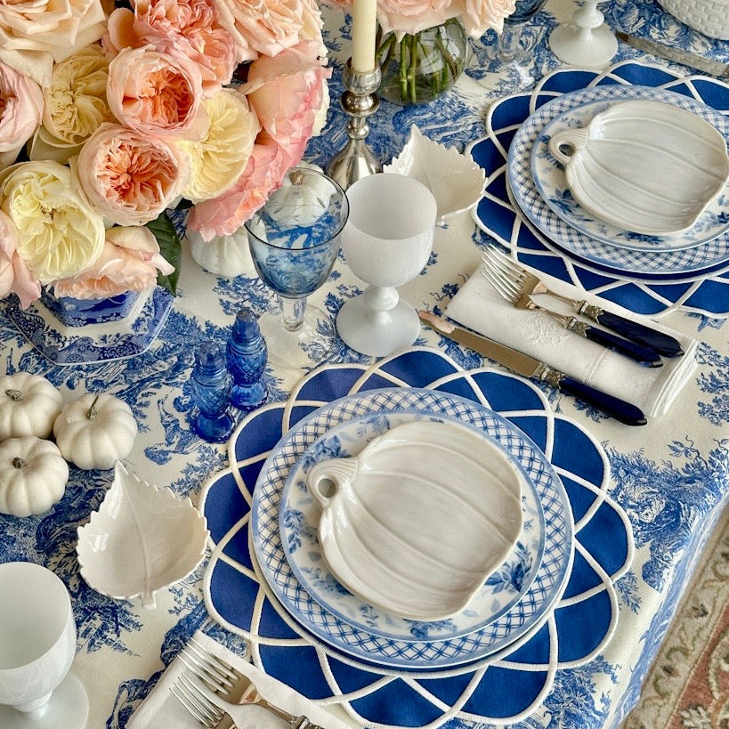Decorative table setting with blue and white plates, pink flowers, and white pumpkins.
