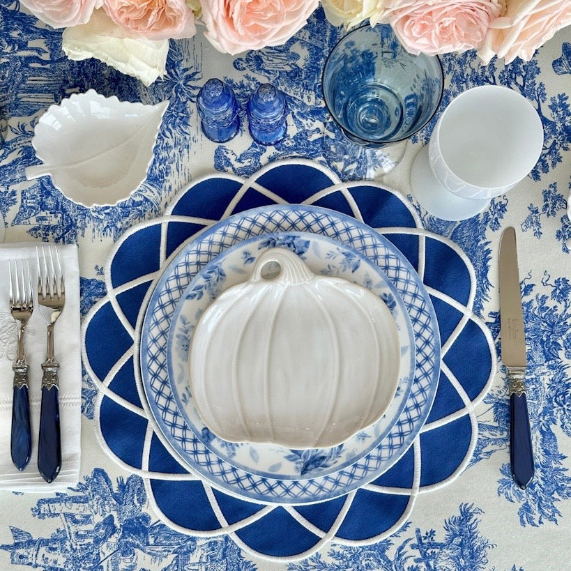 Elegant table setting with blue and white patterned tablecloth, floral centerpiece, and decorative pumpkin.