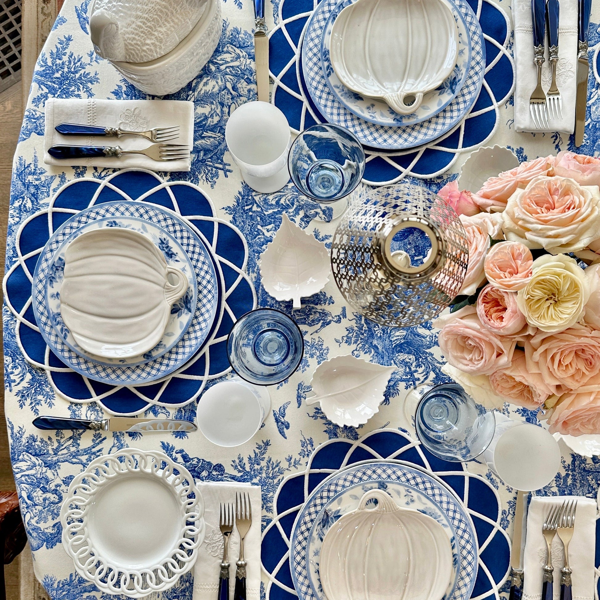 Elegant table setting with blue and white patterns, white pumpkins, and pink flowers.