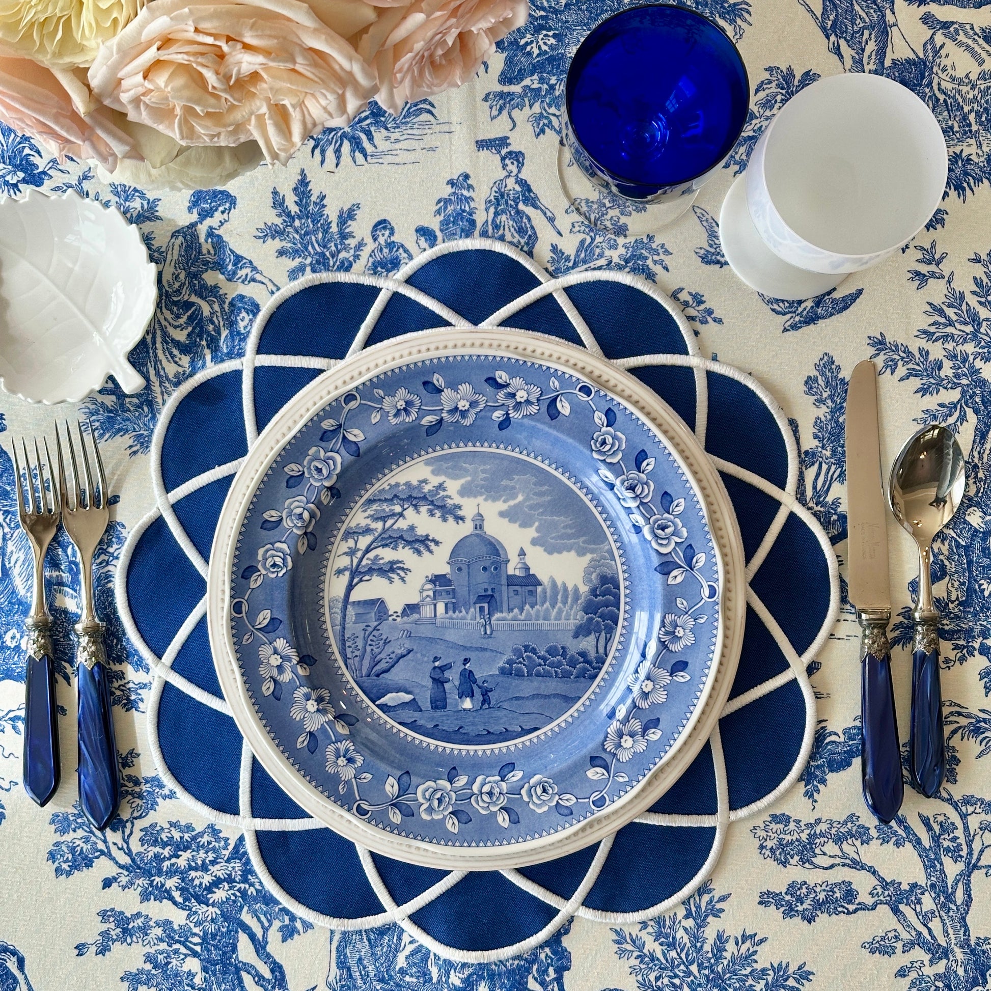 Decorative table setting with blue and white plates, cutlery, and floral arrangements on a patterned tablecloth.