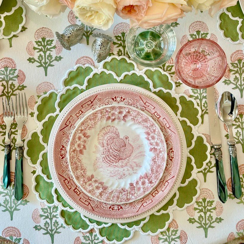 Decorative table setting with pink and white floral arrangement, patterned plates, and cutlery on a matching tablecloth.
